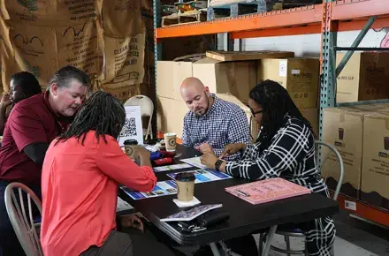 Four community members sit at a table reviewing materials on the table.
