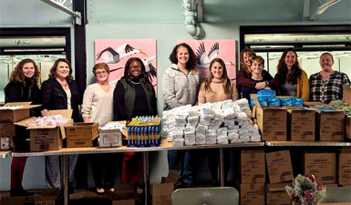 Photo of Women United members standing behind a table piled with supplies to be packed