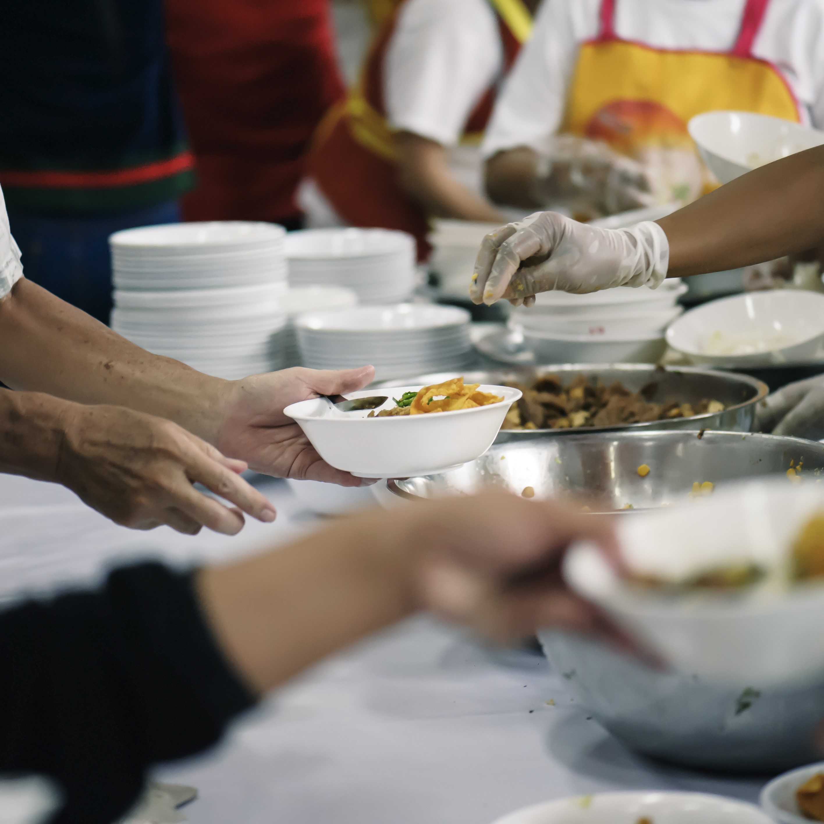 Hands are seen giving and taking bowls of food over a table.\