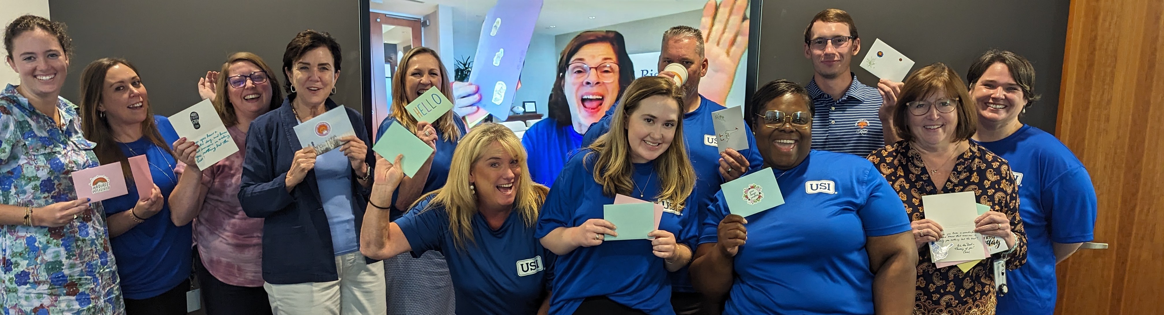 A group of volunteers smile with cards they have written during their volunteer hours.