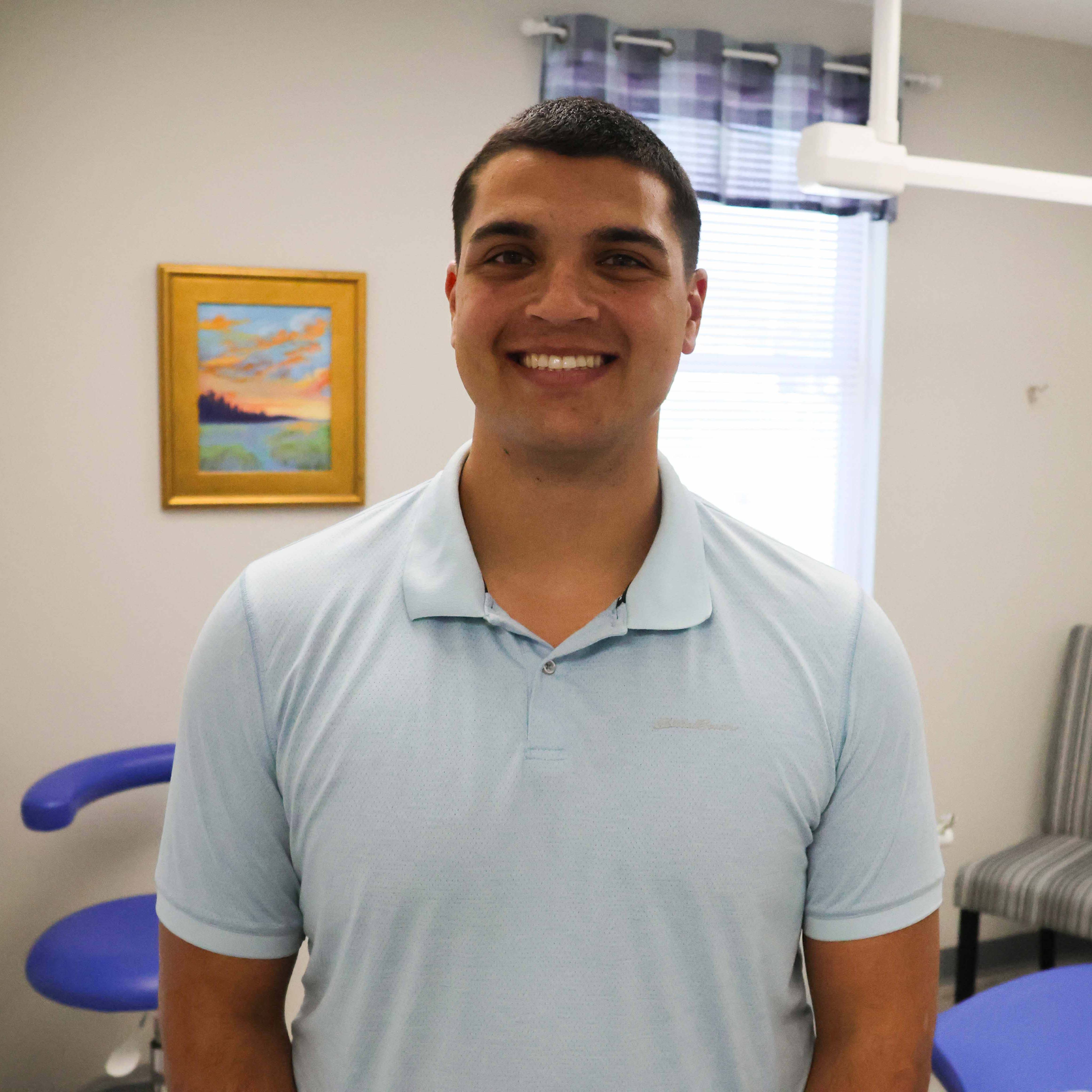 A photo of Elijah Melendez smiling in front of a dentist's chair.