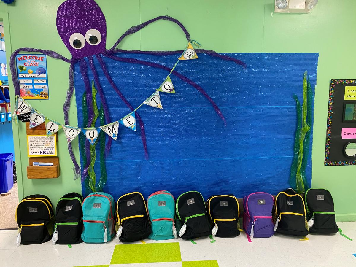 A row of back packs in front of a bulletin board with an octopus