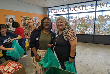 2 members of Women United pose for photos while packing bags for backpack buddie at lowcountry food bank.