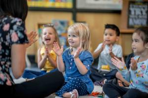 A teacher claps with students while smiling.