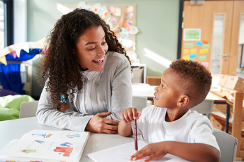 A child and teacher smile while doing an activity in the classroom.