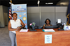 Photo of the inside of the berkeley resource connection center at the reception desk. One woman is standing next to the desk, another woman is sitting behind the desk. Both are smiling looking at the camera.