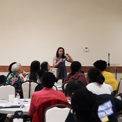 Laura Fogle speaks into a microphone presenting to a group of people at a SafetyNet meeting