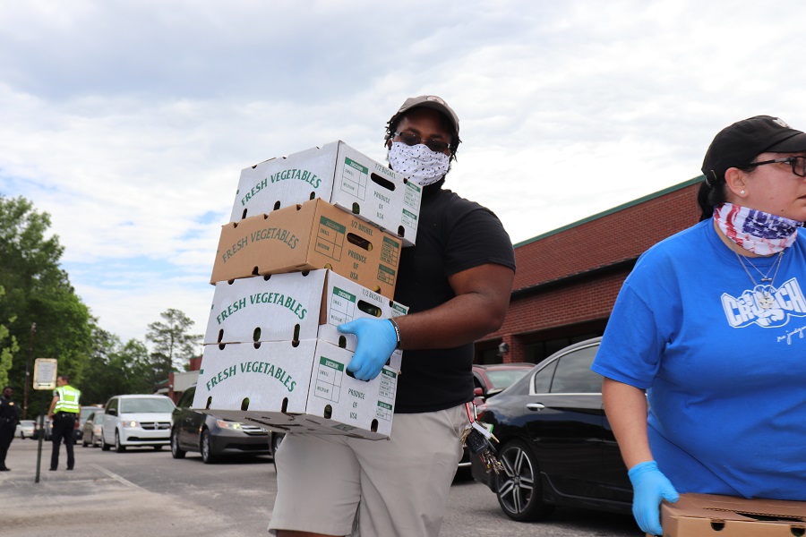 volunteer with mask and gloves on carrying 4 boxes of fresh produce