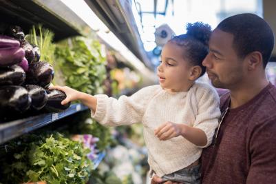 A father and daughter overlook the produce section of a grocery store.