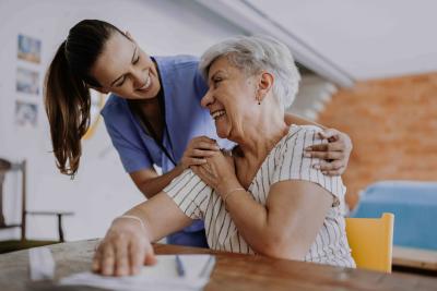 A younger doctor embracing an older woman, both smiling.