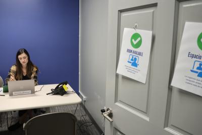 Woman sitting at laptop computer in conference room. There are signs on the door in Spanish and English that say room available