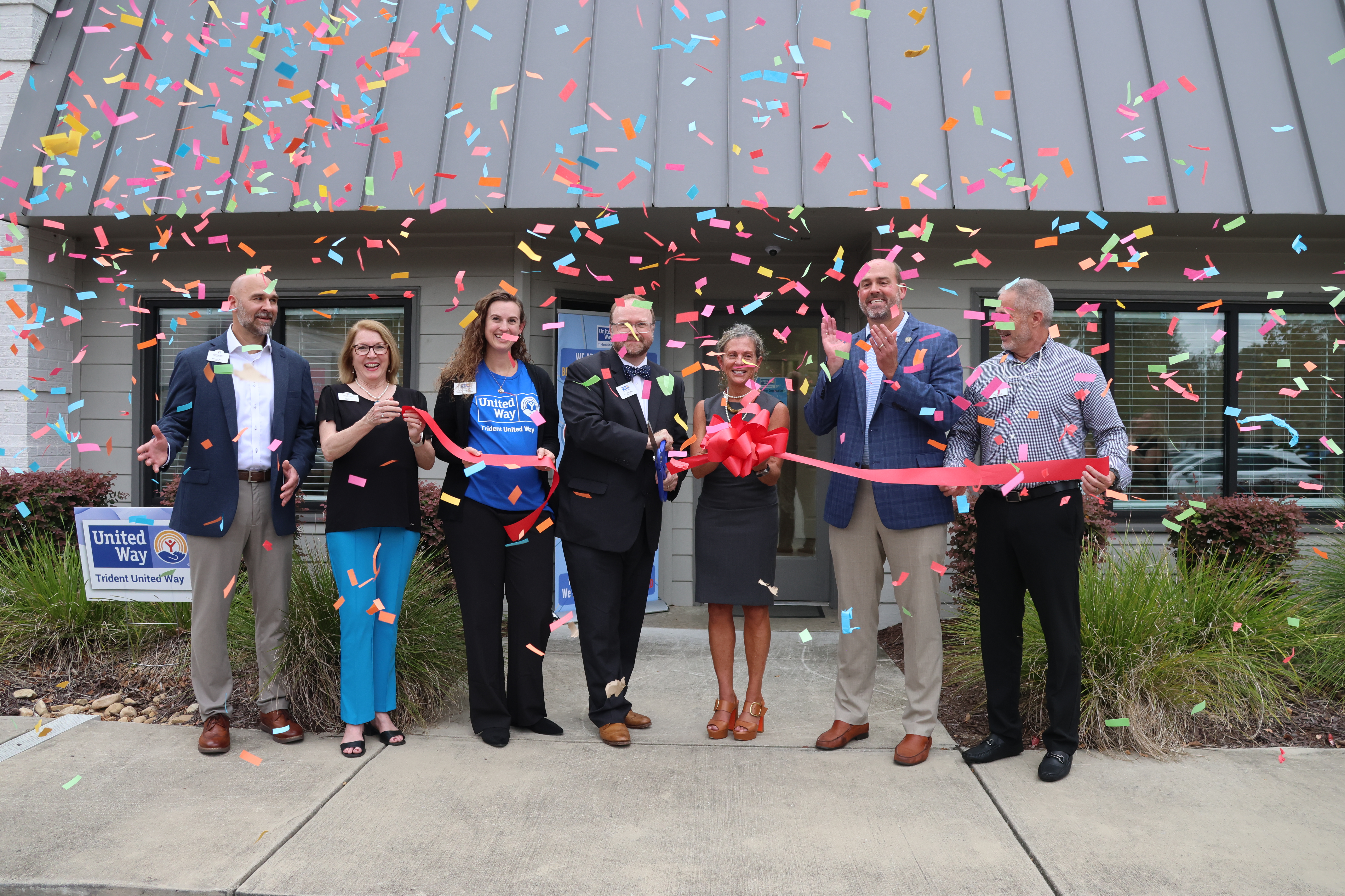 A group of Trident United Way representatives stand beneath confetti while they cut the ribbon for the new Dorchester Resource Connection Center Location.