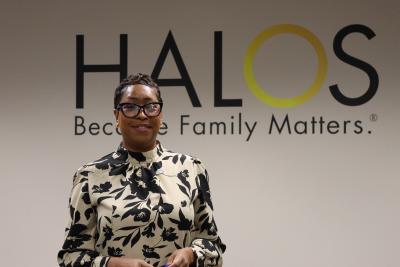 Director of Programs Khalilah Sumners stands in front of the HALOS logo on a wall.