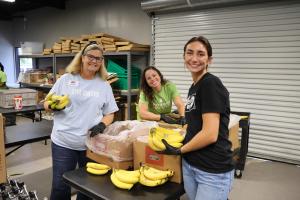 Three volunteers posing for the camera at FoodShare. Two are holding bunches of bananas