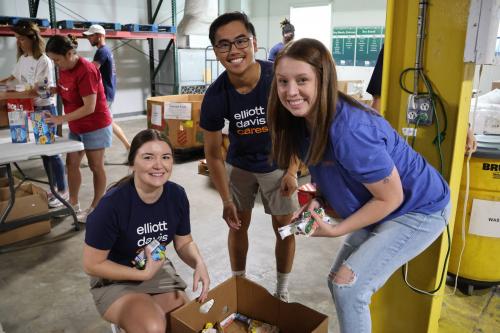 three volunteers from Elliott Davis smile for the camera while sorting boxes of donated food items