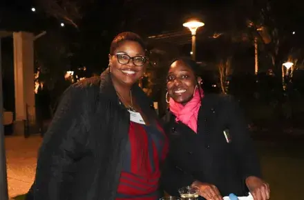 Two women are standing and smiling at the camera at a table with oysters