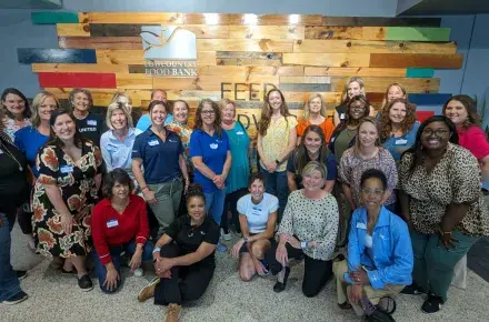 A large group of women pose for a picture in front of a sign for Lowcountry Food Bank