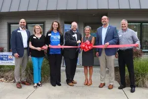 Seven individuals stand outside of the Dorchester Resource Connection Center holding a ribbon for the grand opening