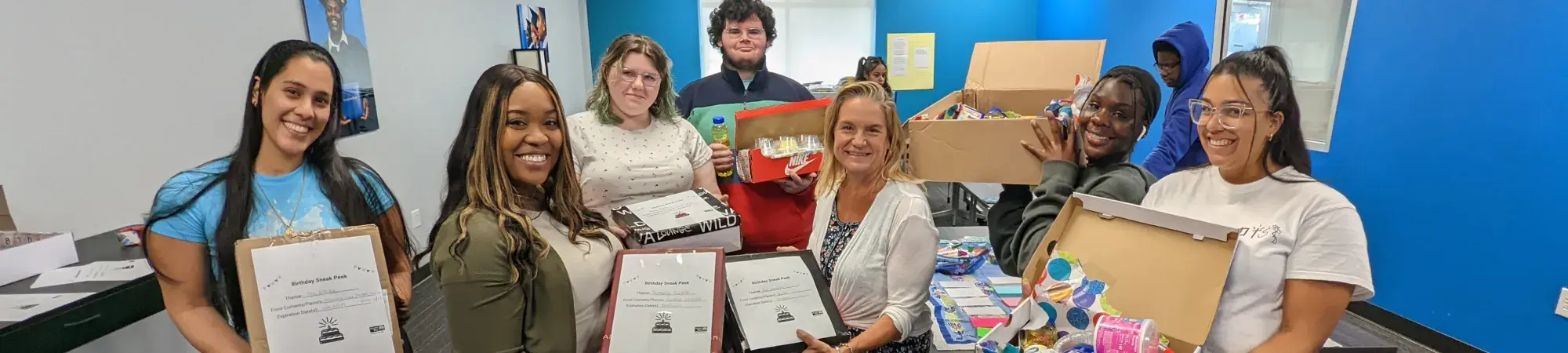 A group of individuals smiling at the camera holding birthday boxes