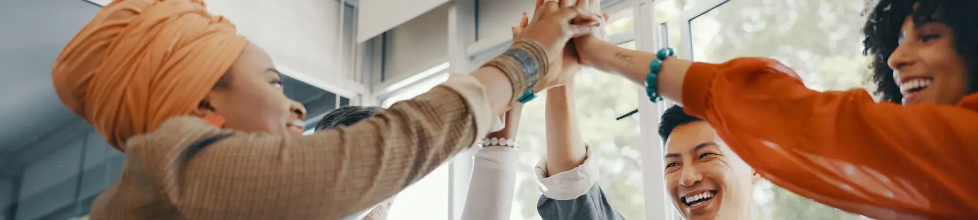 Four diverse people smile and highfive together