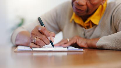 A woman writes on paper, she is sitting at a table.