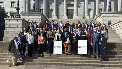 A group of United Way employees pose outside with their logo signs.