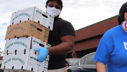 volunteer with mask and gloves on carrying 4 boxes of fresh produce