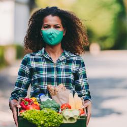 woman wearing mask and holding box containing food