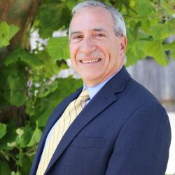 Photo of Trident United Way CFO David Wasserman. He is wearing a blue button down with a navy suit jacket and a yellow tie. David has short gray hair. 