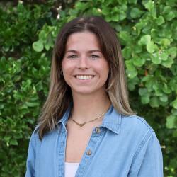 Photo of Angela Hiltbrunner, outside in front of tree, smiling. She is wearing a chambray top and a gold necklace.