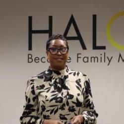 Director of Programs Khalilah Sumners stands in front of the HALOS logo on a wall.